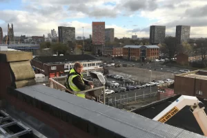 Engineer manning a cherry picker on a rooftop overlooking Manchester.
