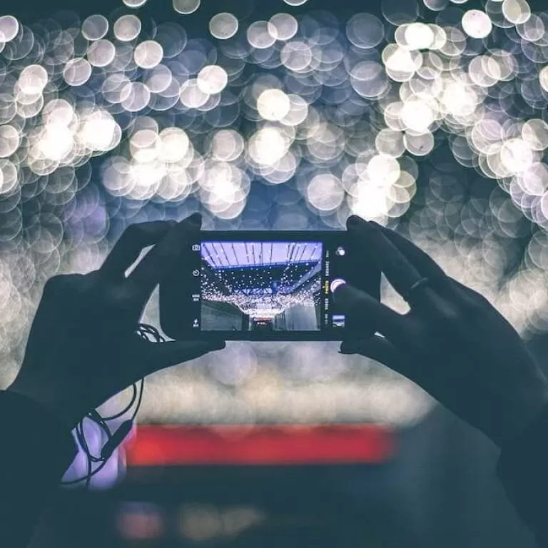 Image of two hands holding a smartphone, about to take a photograph of a picturesque scene of colourful lights.