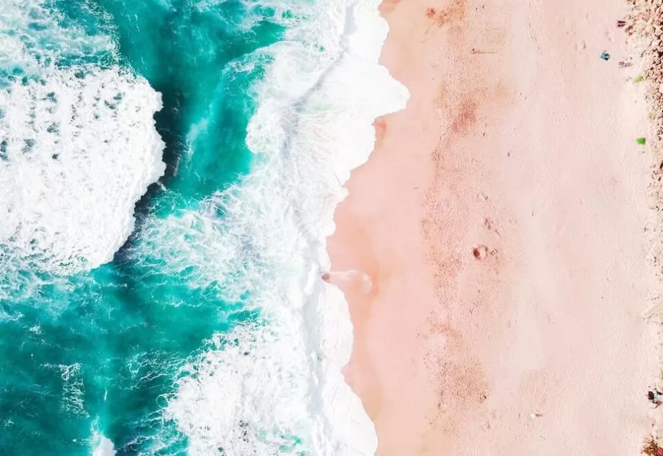 Aerial perspective of waves crashing onto a sandy beach.
