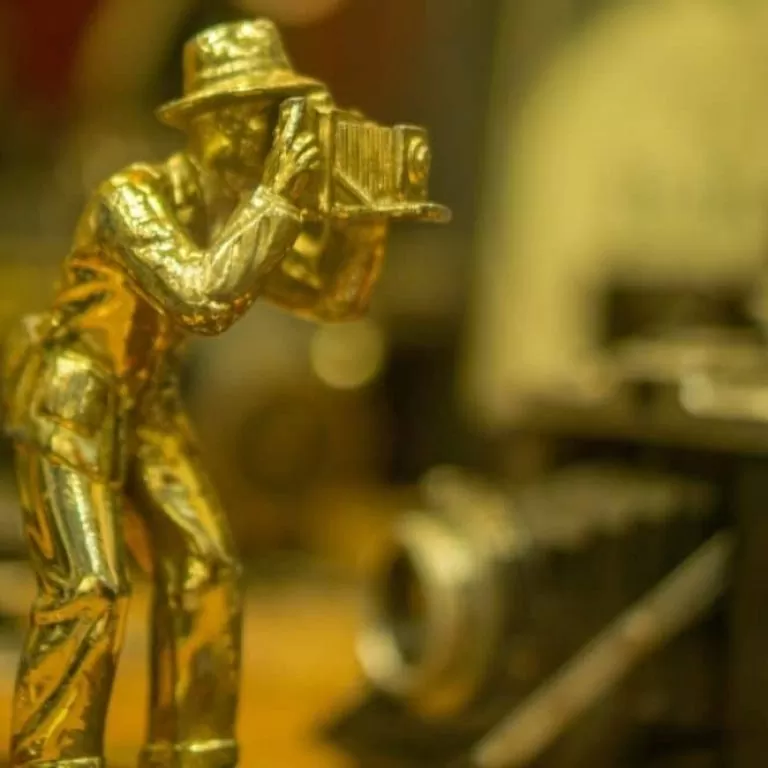 A gold antique miniature statue of a man taking a photograph with a vintage camera