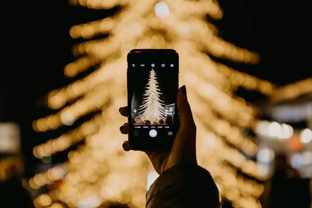 The view from a smartphone camera as it frames a photograph of a well-lit Christmas tree.