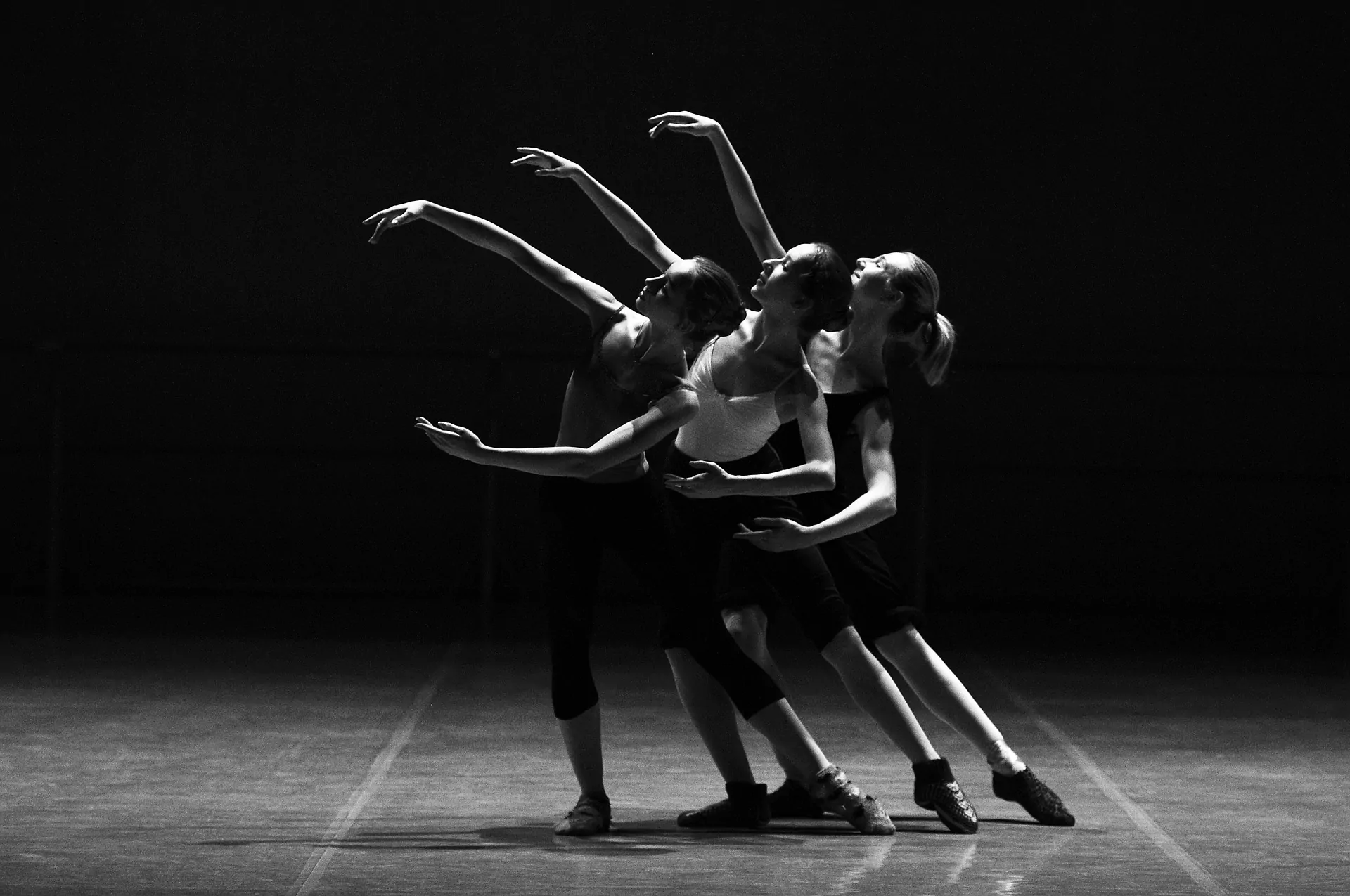 Ballerinas dancing on a stage in unison. This black and white image shows three ballerinas lifting their arms in time. Time-lapse of theatres.