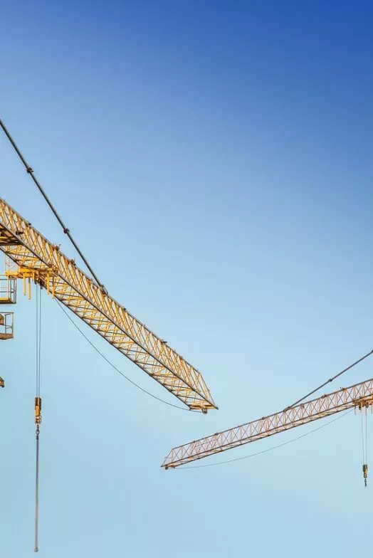 An image of two cranes against a bright blue sky
