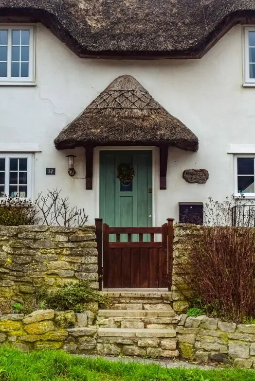An image of an English cottage. The thatched roof and porch are characteristic of historic builds in this area.