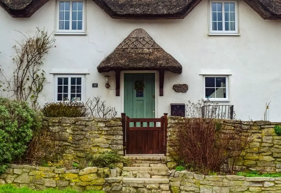 An image of an English cottage. The thatched roof and porch are characteristic of historic builds in this area.