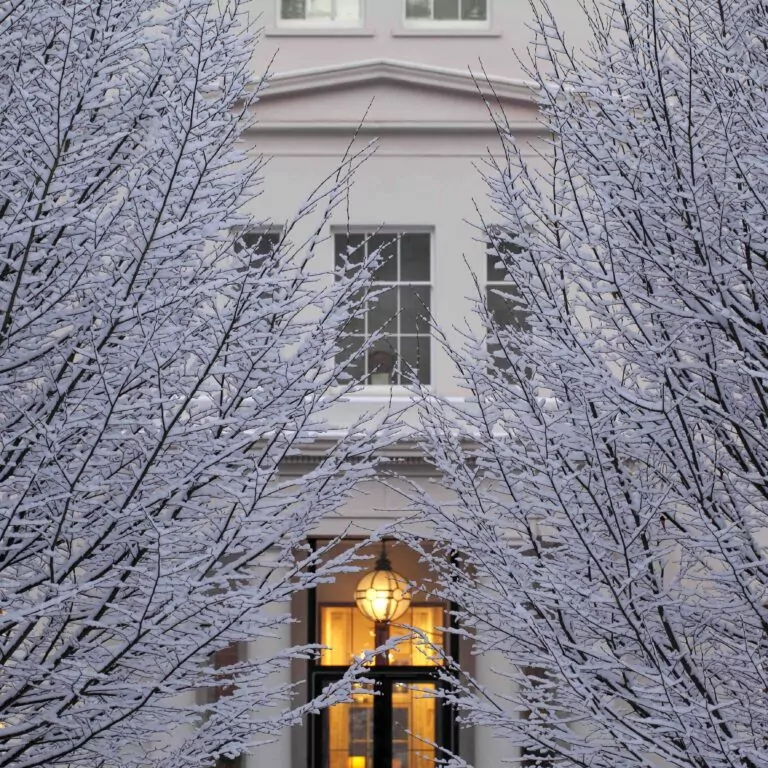An exterior image of Coworth Park. Bare branches are covered in snow in this stunning winter scene.
