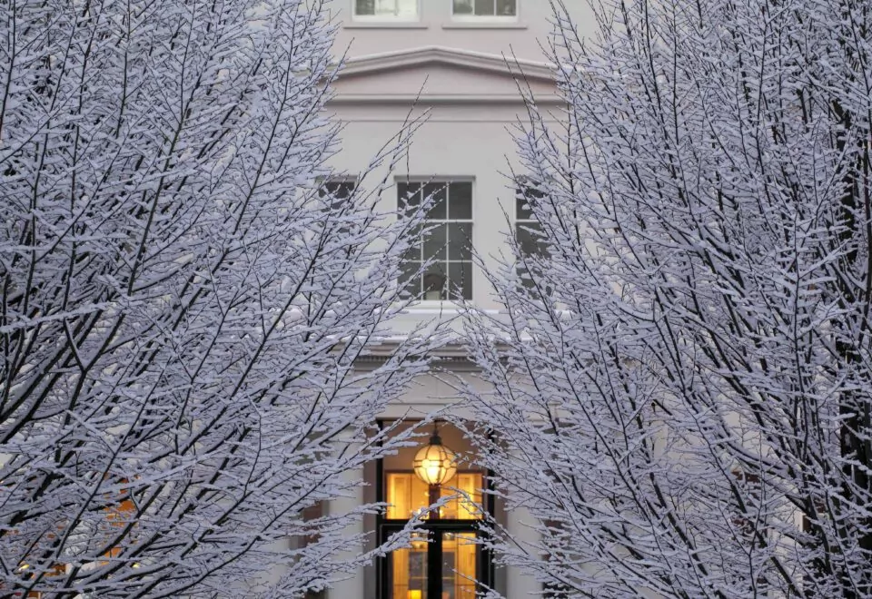 An exterior image of Coworth Park. Bare branches are covered in snow in this stunning winter scene.